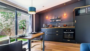 A modern kitchen with dark cabinetry, a wooden countertop, and a built-in oven. There is a dining area with a table and chairs, and a view of a garden through large windows.