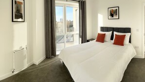 Ein Schlafzimmer mit einem großen Bett, zwei Kissen, einem Heizkörper, einem Fenster mit Vorhängen und einer Tür zum Badezimmer.