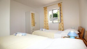A hotel room with two beds, a window with curtains, a bedside lamp, and a wardrobe. - Apartments Dubreta - Superior Two Bedroom Apartment With Balcony (Konavle)