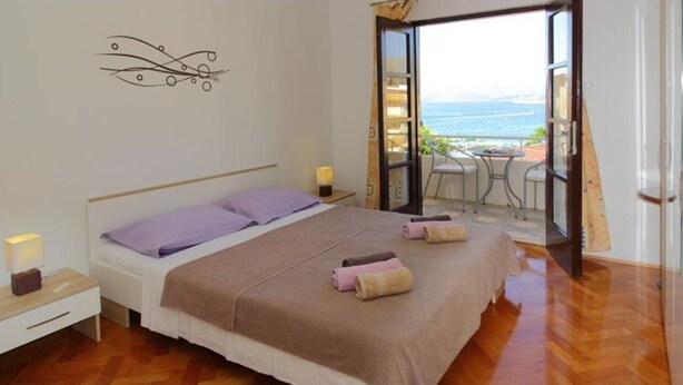 A bedroom with a bed, a nightstand, a decorative wall piece, and a balcony with a view of the sea. - Apartments Dubreta - Superior Two Bedroom Apartment With Balcony (Konavle)