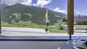 Vue depuis un espace extérieur abrité, avec une table et des chaises, donnant sur un paysage montagneux sous un ciel dégagé.