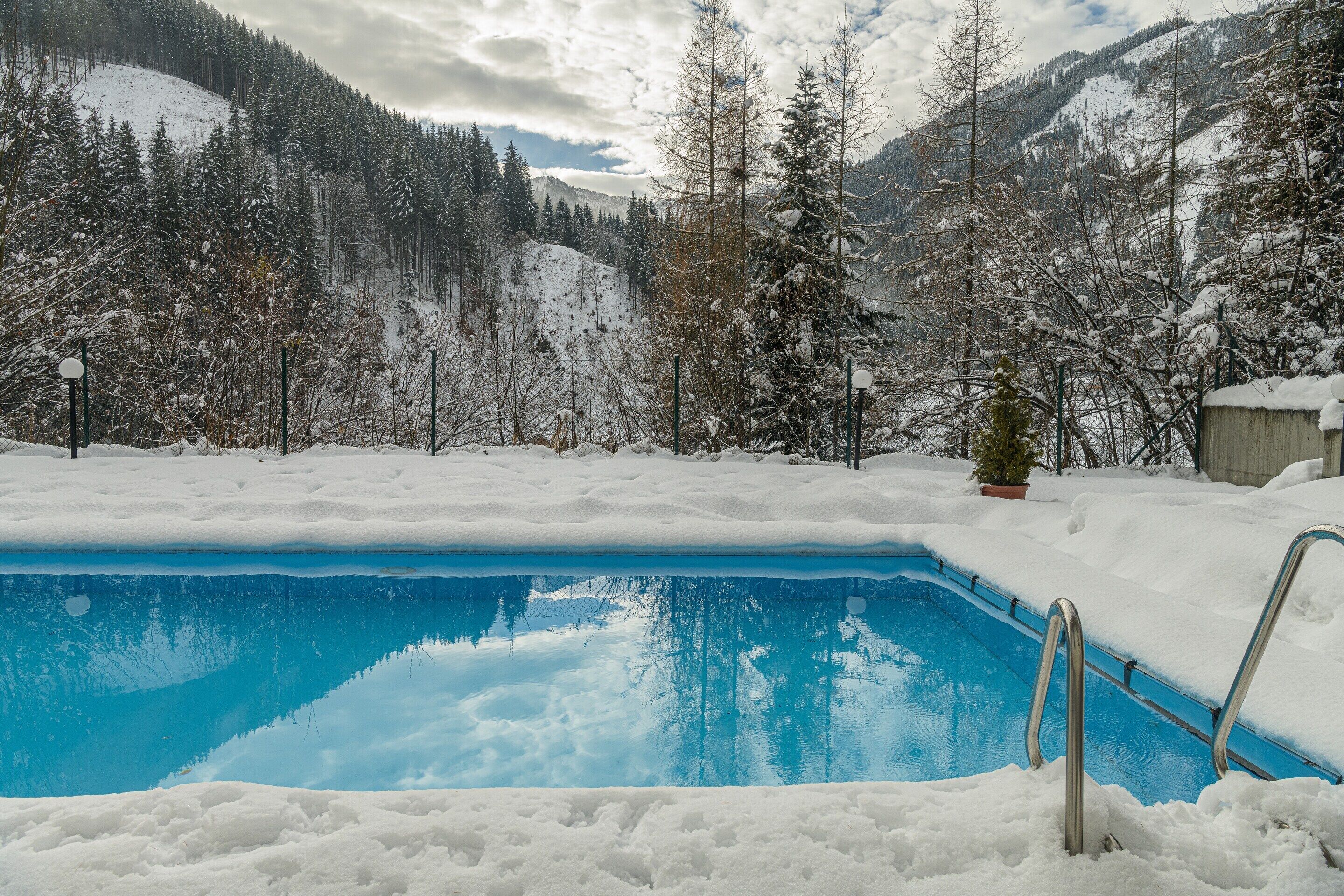 Una piscina rodeada de árboles nevados y montañas.
