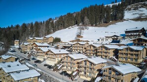 Un village de montagne enneigé, avec des bâtiments à plusieurs étages, un télésiège et une route.