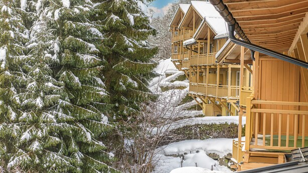 Une cabane en bois dotée de plusieurs balcons, entourée d’arbres couverts de neige.