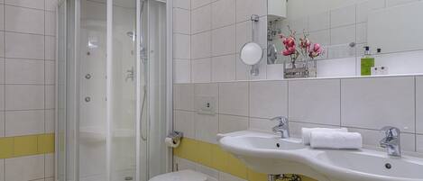 Un baño con ducha, inodoro y dos lavamanos.