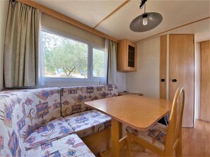 Ein kompaktes Wohnmobil-Interieur mit Holztisch, Sitzbank, einem Fenster mit Vorhängen und einem Schrank.