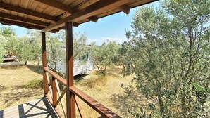Eine Holzterrasse mit Blick auf Olivenbäume und ein entferntes Gebäude.
