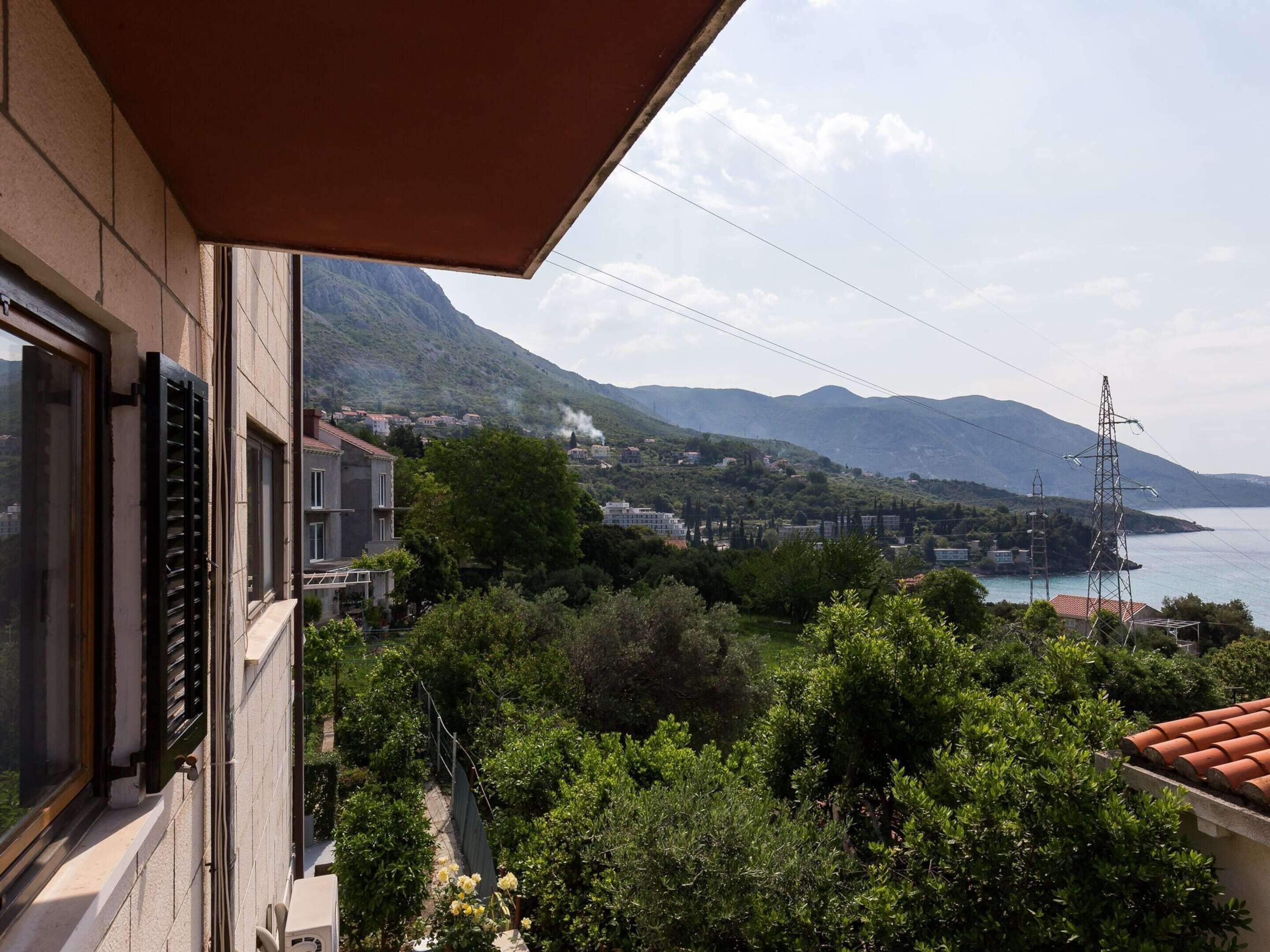 Un balcon offrant une vue sur un paysage montagneux, une étendue d’eau et un pylône de ligne électrique.