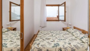 Un dormitorio con dos camas, una ventana que da a un edificio con tejas rojas y un espejo en la pared izquierda.