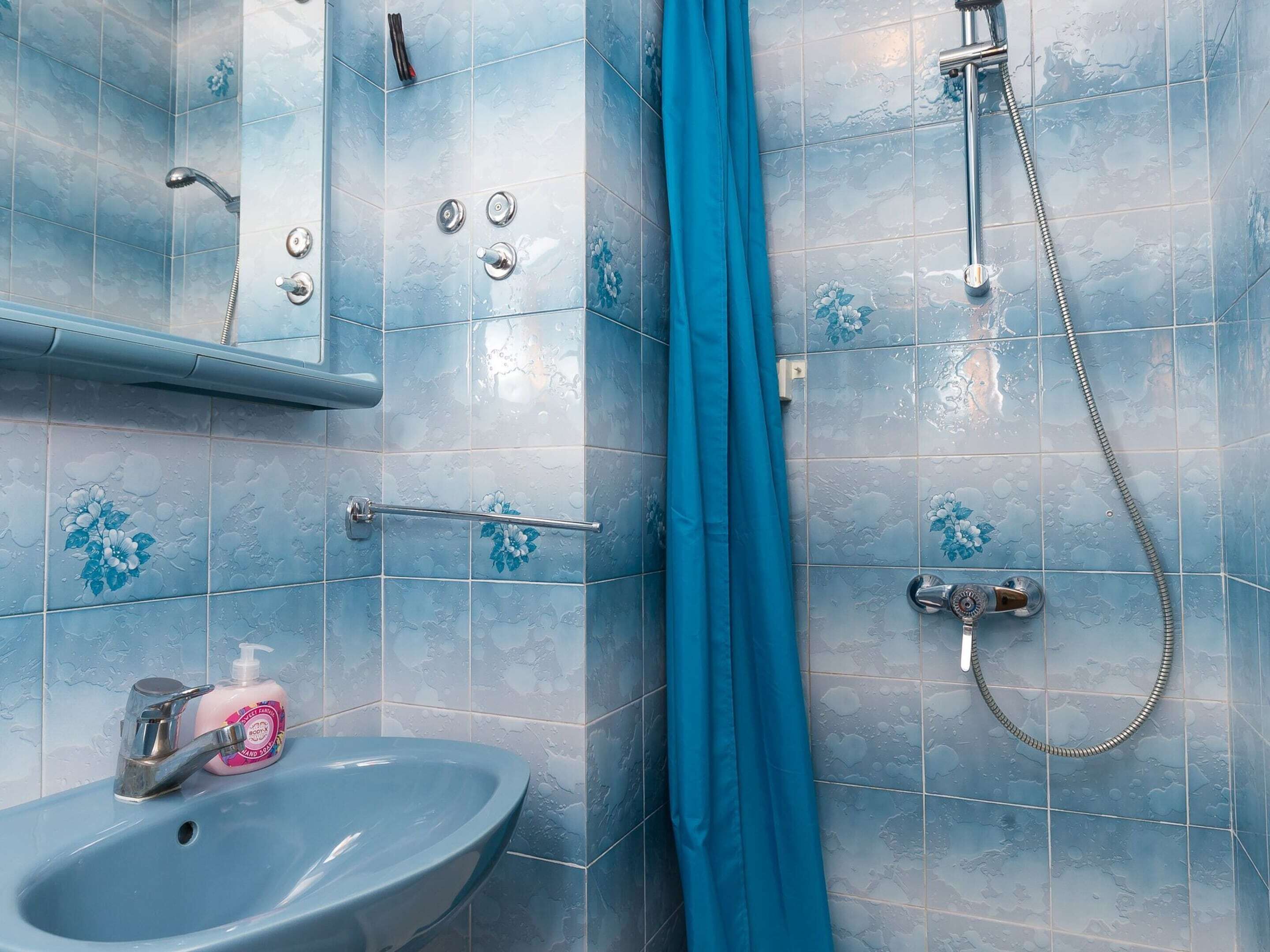 Une salle de bain avec un lavabo, un miroir, une douche et un rideau bleu.
