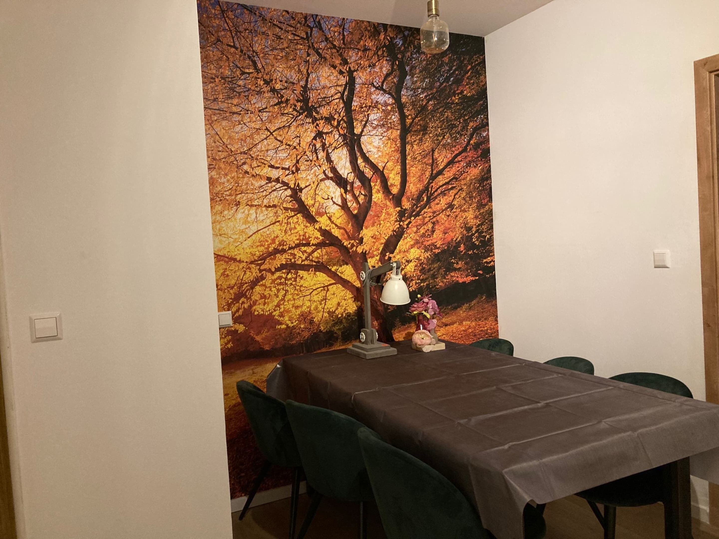 A dining area with a table set for four, a lamp, and a vase with flowers.