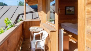 Varanda de madeira com mesa, cadeira, cama e janela com vista para o céu.