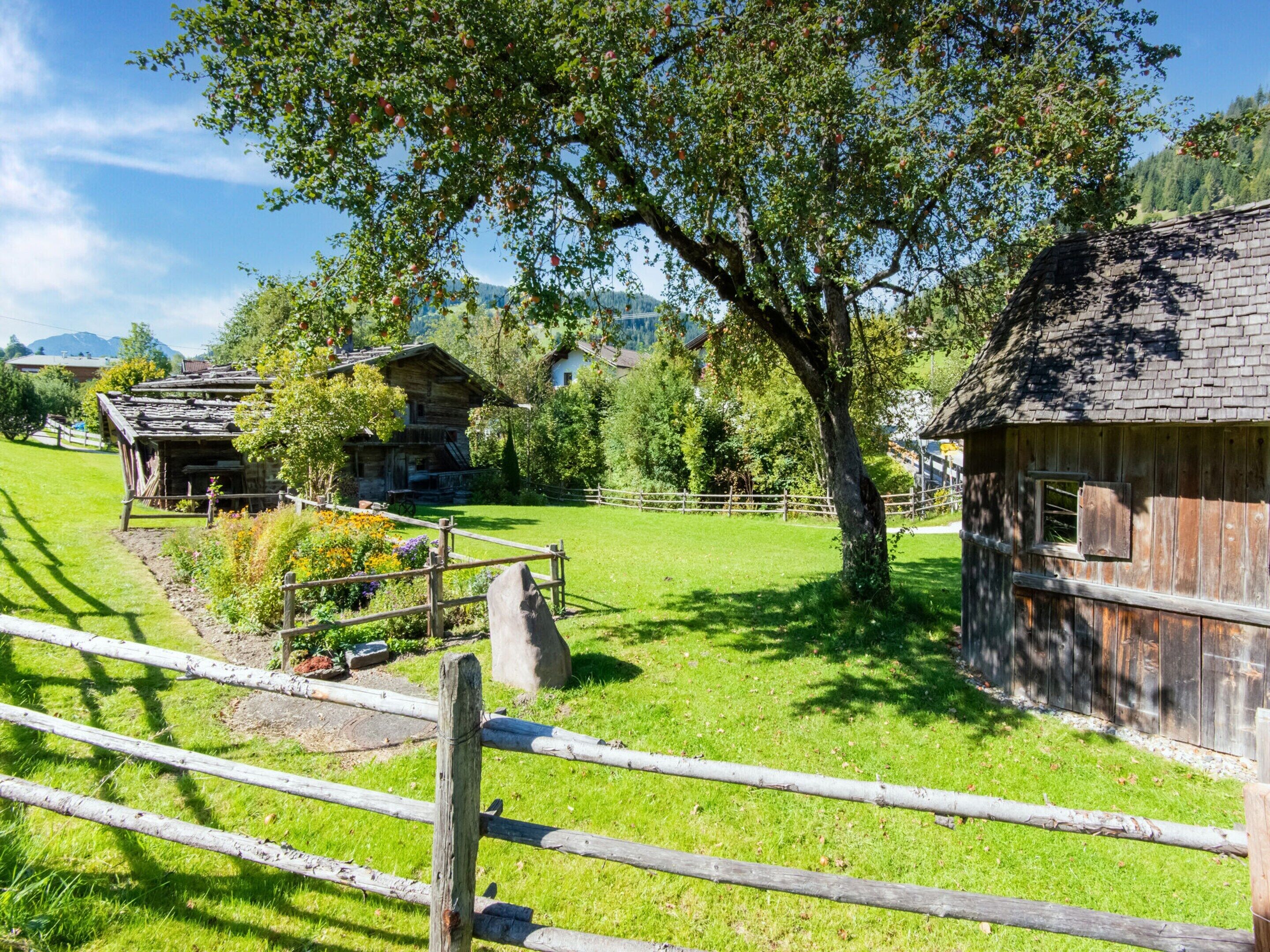 Un rustico chalet in legno con tetto di paglia, circondato da una recinzione in legno e vegetazione lussureggiante.