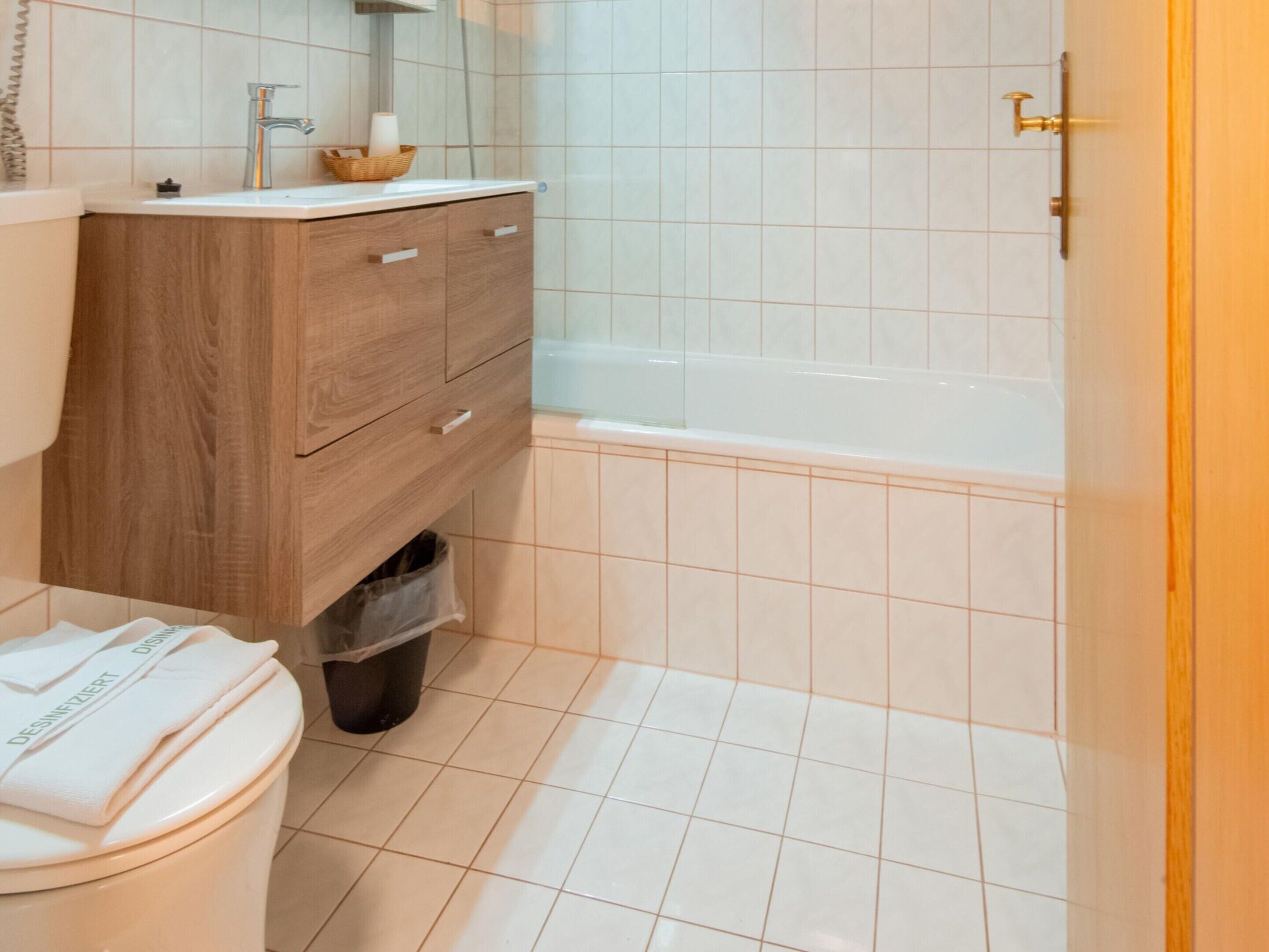 A bathroom with a wooden vanity, a white sink, a mirror, a white toilet, and a bathtub.
