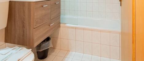 A bathroom with a wooden vanity, a white sink, a mirror, a white toilet, and a bathtub.