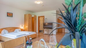 A hotel room with a bed, a TV, a shower, and a dining table with fruits and a vase. - Apartment in Neustift Near Ski Lift (Neustift Im Stubaital)
