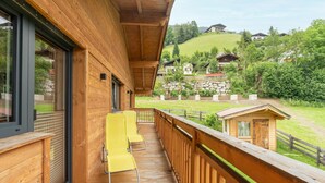 Een houten balkon met gele stoelen, een stenen muur en uitzicht op huizen op een heuvel.
