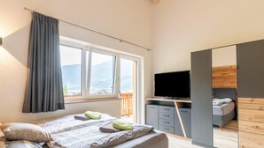 Een slaapkamer met een bed, een televisie, een kledingkast en een balkon met uitzicht op bergen.