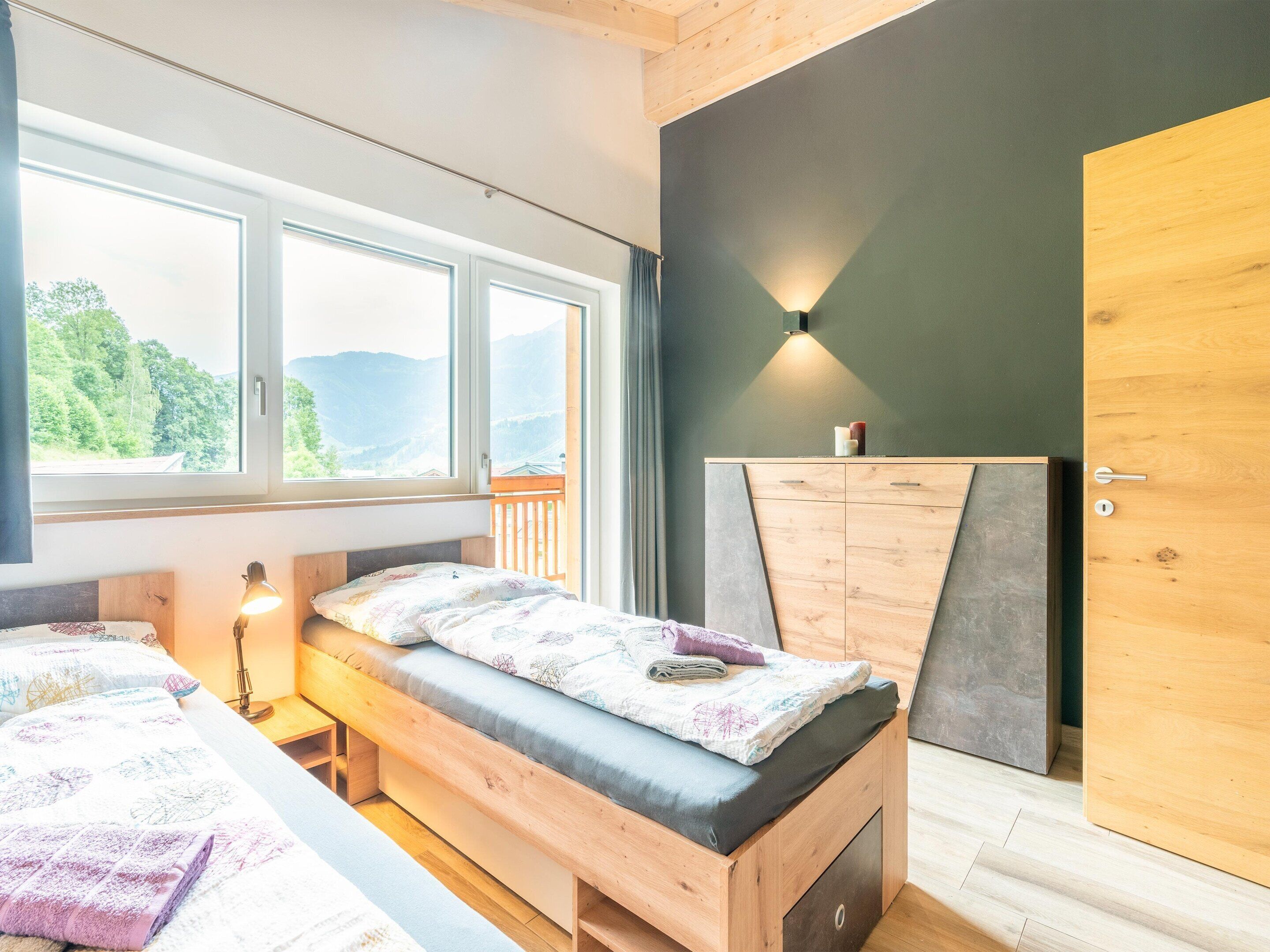 Ein Schlafzimmer mit Bett, Nachttisch und Blick auf Berge durch große Fenster.