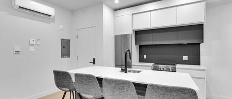 A modern kitchen with white cabinetry, a central island with bar stools, a stainless steel refrigerator, and a black backsplash.