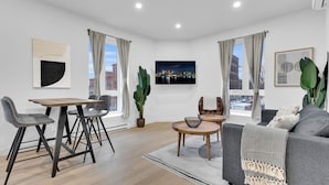 Een moderne woonkamer met een eethoek, een grijze bank en een groot raam met gordijnen.