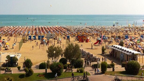 Een strand met rijen ligbedden en parasols, een speeltuin en enkele mensen die wandelen.