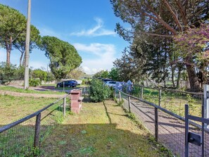 A fenced outdoor area with a paved walkway, trees, and parked cars.