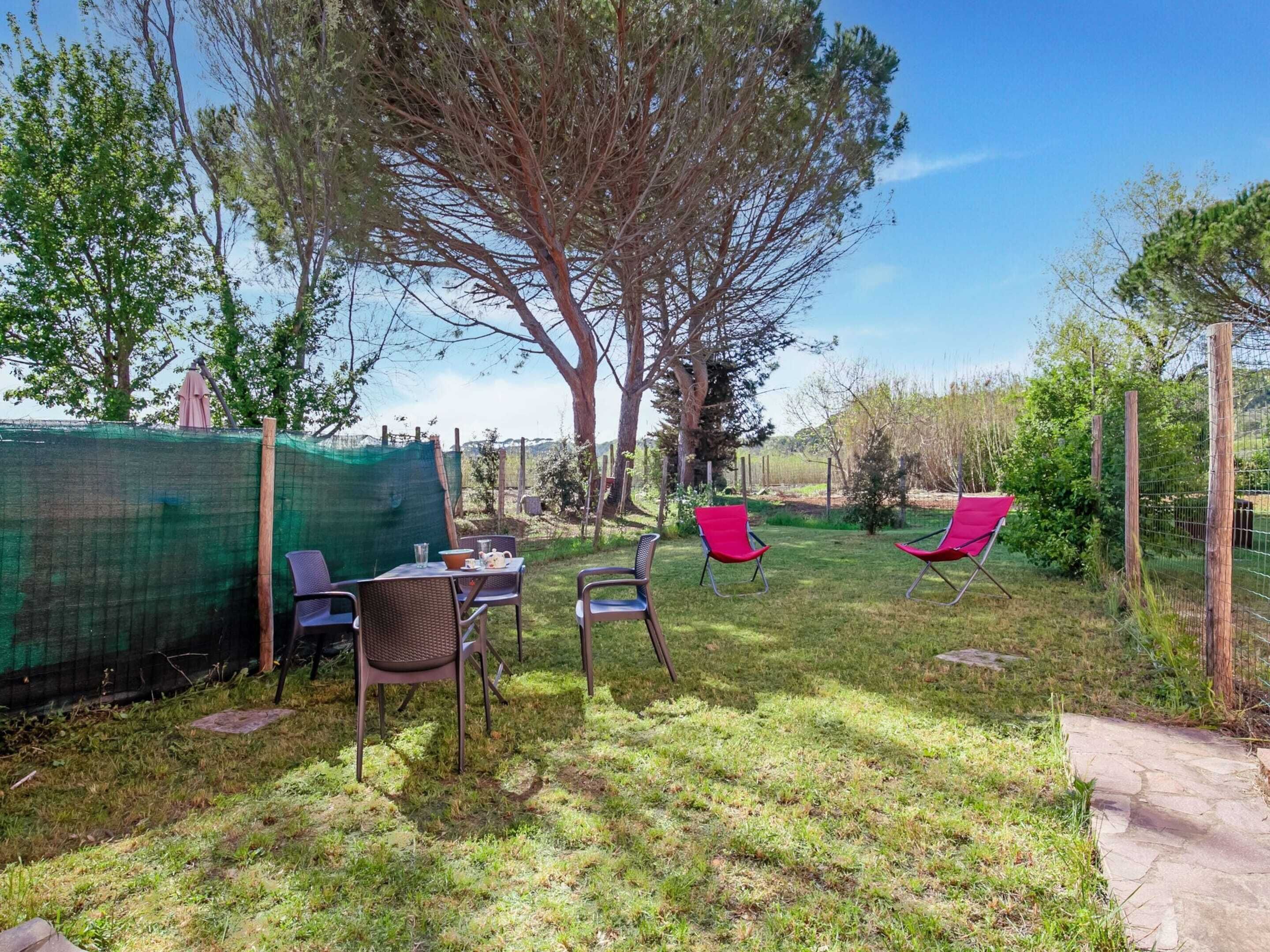 A backyard with a table and chairs, a large tree, and a fenced area.