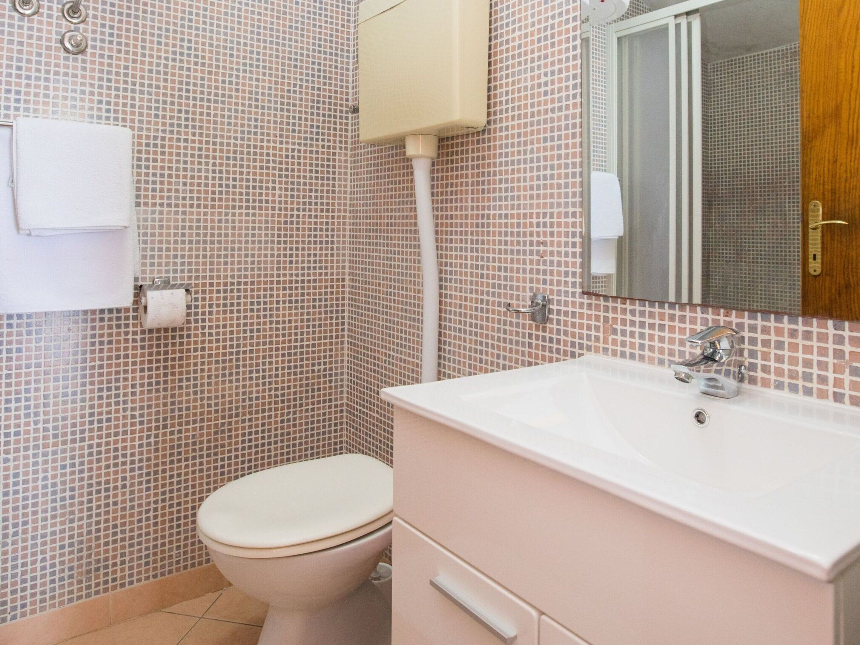 Ein Badezimmer mit Toilette, Waschbecken, Spiegel und Fliesen.