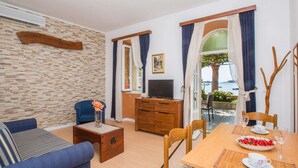 Uma sala de estar com sofá, televisão, um armário de madeira e um espaço de jantar com mesa posta para dois.