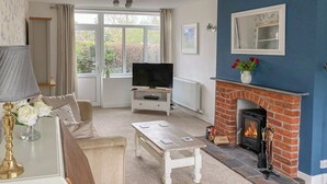 A living room with a television, sofa, coffee table, fireplace, and a view of the outdoors through large windows. - 3 bedroom accommodation in Rugby (Rugby)