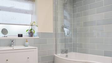 Une salle de bain avec une baignoire, une douche, une fenêtre avec une plante et un meuble-lavabo avec des tiroirs.