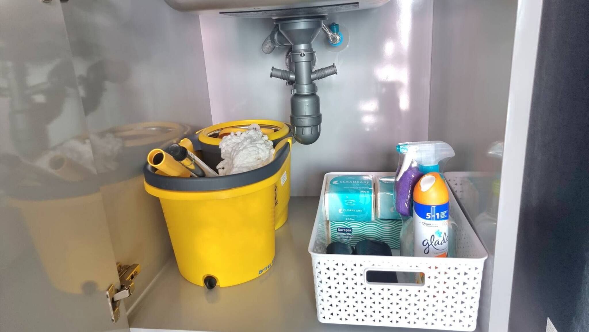 A bathroom sink with a yellow cleaning bucket, a white laundry basket, and cleaning supplies.