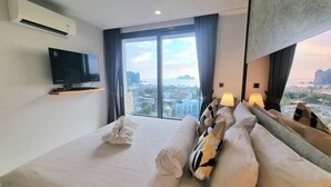 A hotel room with a large bed, a flat-screen TV, a view of the cityscape, and a window with curtains. - Bo501 - 2 Bdr Condo With Sea View, Ao Nang Beach (Krabi)