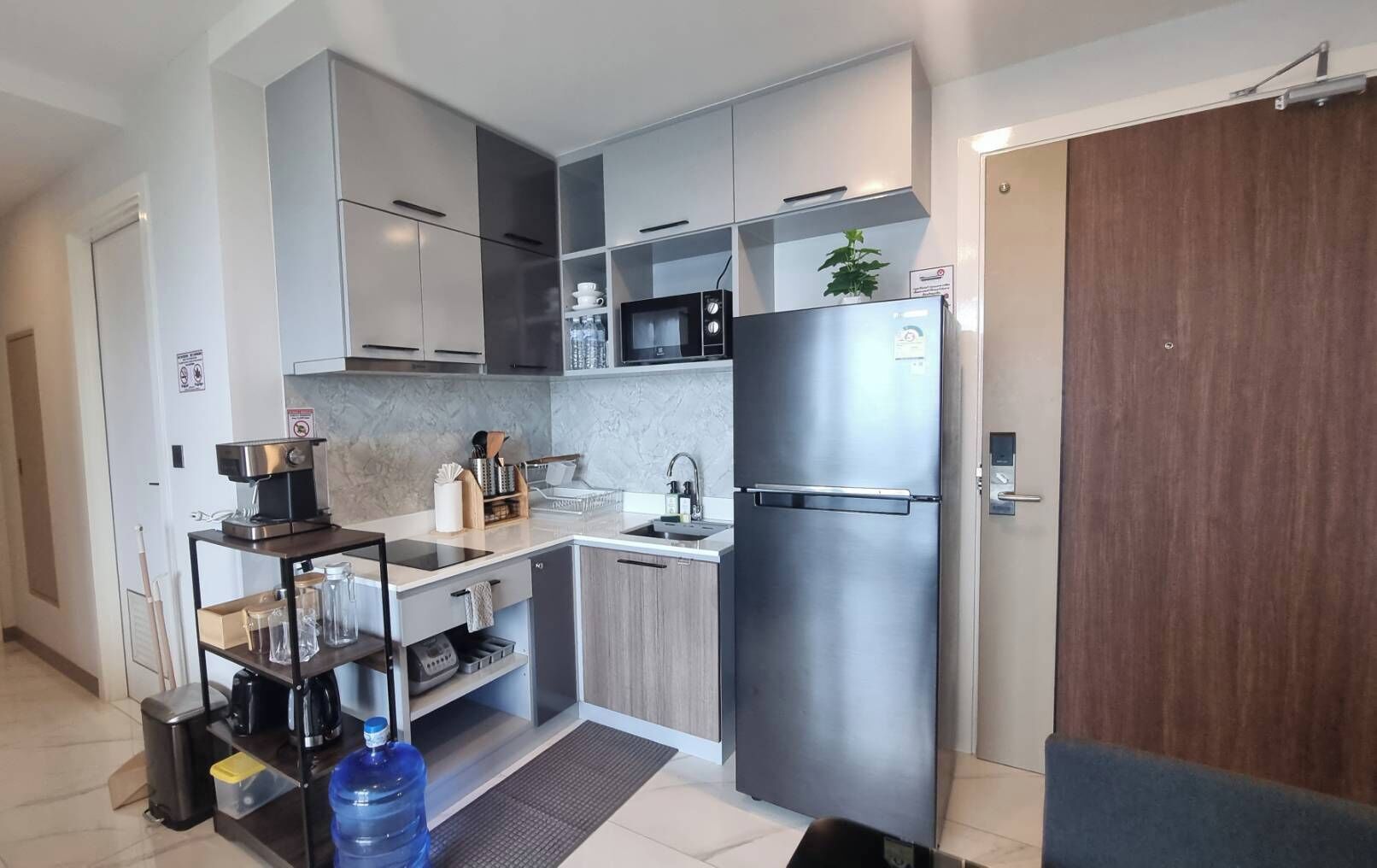 A modern kitchen with grey cabinets, a stainless steel refrigerator, a microwave, and a coffee machine.