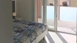Un dormitorio con cama, mesita de noche y vistas al mar a través de un ventanal corredero.
