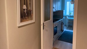 Pasillo que conduce a una cocina con comedor, un cuadro en la pared y una puerta con panel texturizado.