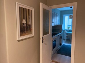 Pasillo que conduce a una cocina con comedor, un cuadro en la pared y una puerta con panel texturizado.