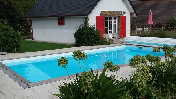 A house with a swimming pool, surrounded by greenery and a patio area.