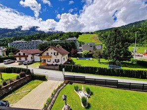 A hotel with a traditional European architectural style, a well-maintained lawn, and a view of the surrounding mountainous landscape.