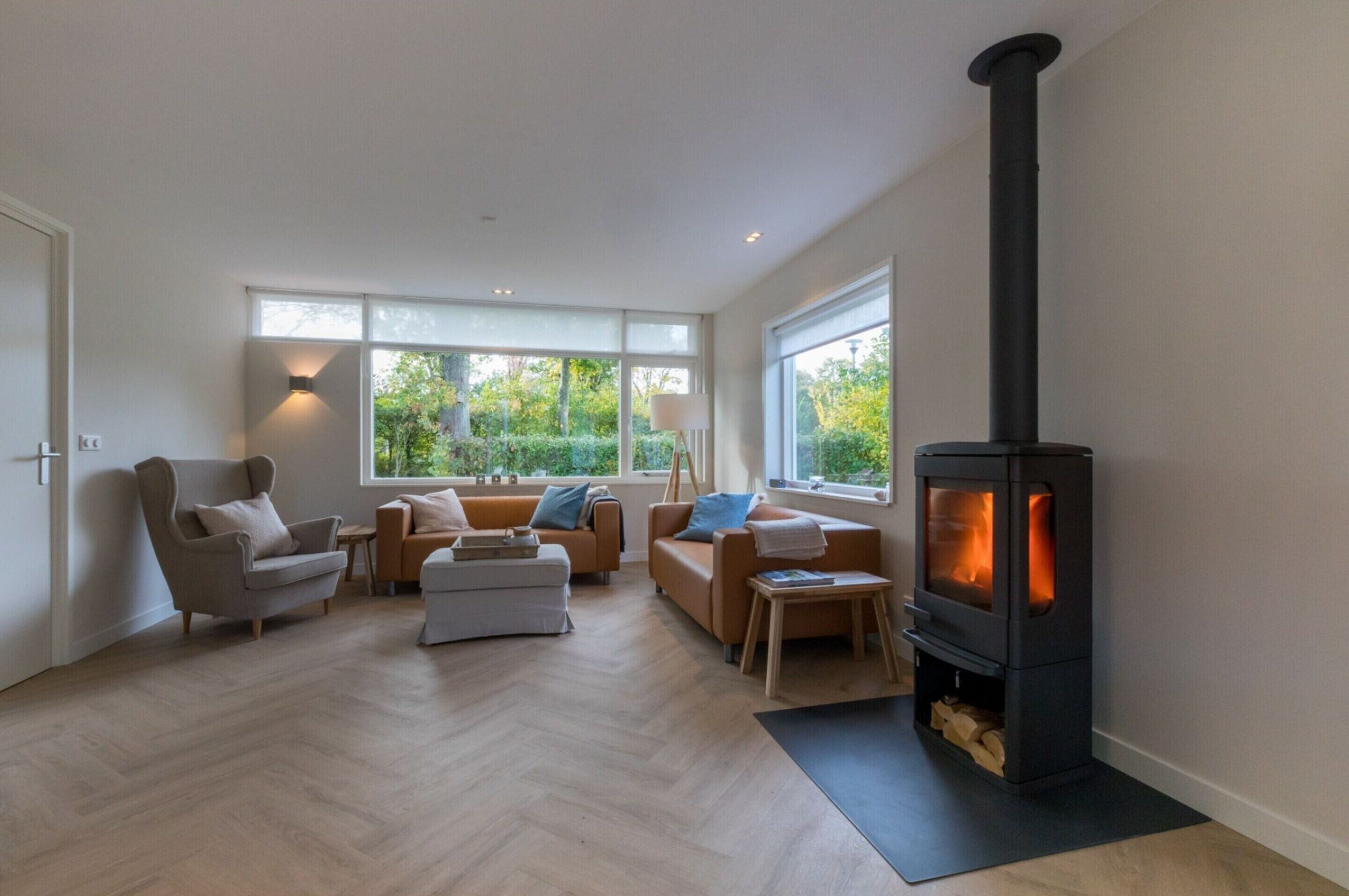 A modern living room with a black wood-burning stove, large windows, and a herringbone floor.
