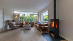 A modern living room with a black wood-burning stove, large windows, and a herringbone floor. - House in Oostkapelle Near Beach & Sauna (Oostkapelle)