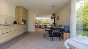A modern kitchen with wooden cabinets, a dining area with a table and chairs, and a view of greenery outside. - House in Oostkapelle Near Beach & Sauna (Oostkapelle)
