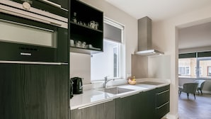 Une cuisine moderne avec des meubles de couleur sombre, un plan de travail blanc, un évier encastré et une fenêtre au-dessus de l’évier.