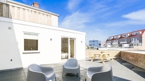 Une terrasse sur le toit, avec des chaises blanches modernes, une table en bois et une vue sur les immeubles résidentiels.