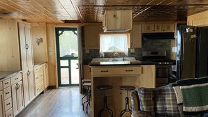 A wooden cabin interior with a kitchen, dining area, and a sofa.