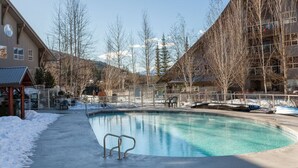 A pool area with a wooden building and a mountain backdrop. - Slope-side condo ski in ski out! Quiet side of resort, heated pool + 3 hot tubs (Whistler)