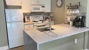 A kitchen with white cabinets, a microwave, a stove, a sink, and a coffee maker. - Slope-side condo ski in ski out! Quiet side of resort, heated pool + 3 hot tubs (Whistler)