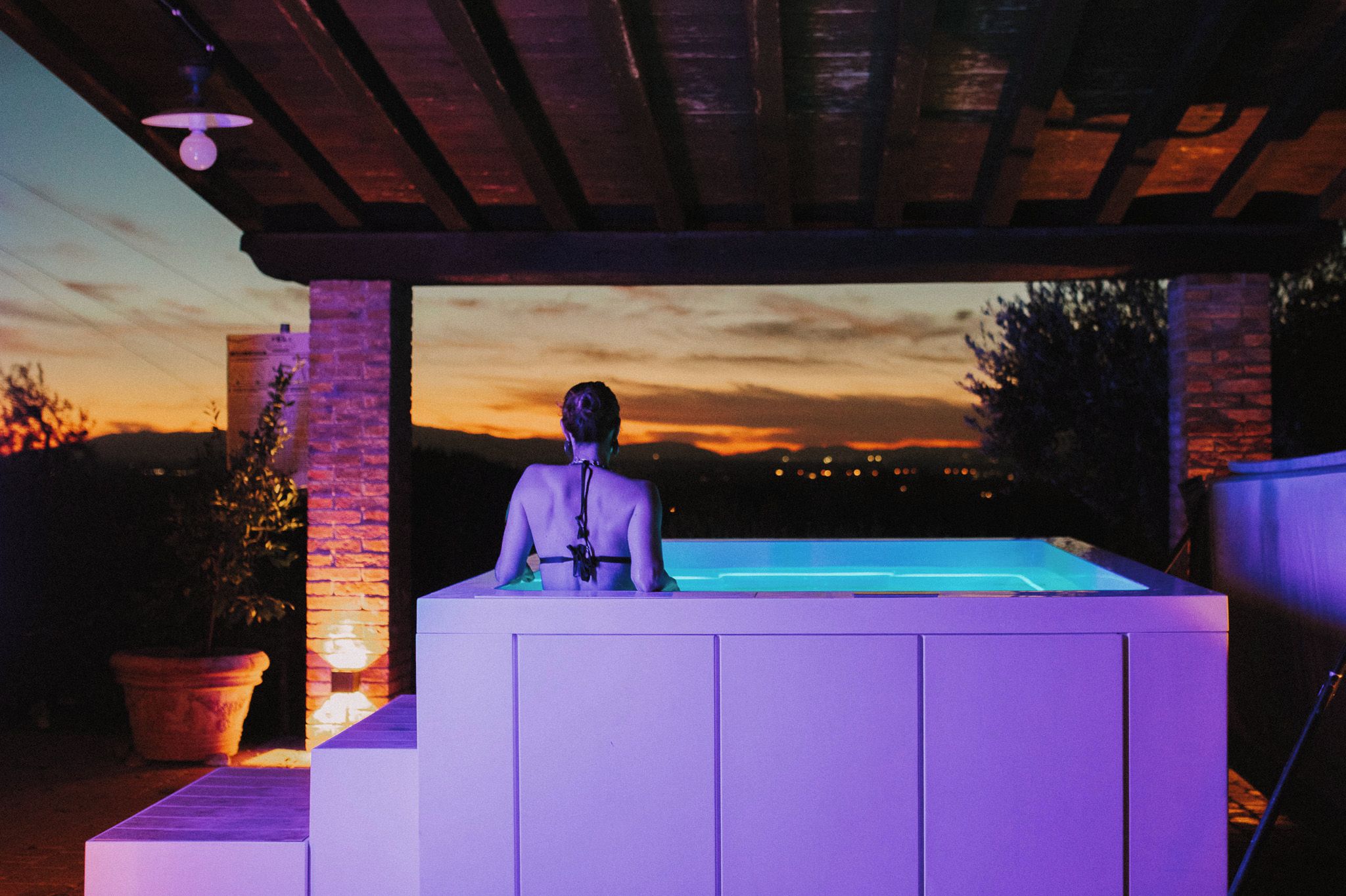 A person standing at a poolside area with a sunset view in the background.