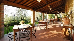 Un patio al aire libre con mesas y sillas de madera, pilares de piedra y plantas en macetas.